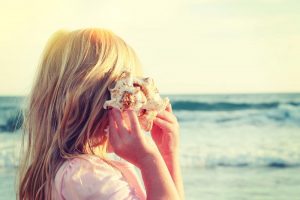 girl holding seashell up to ear at the beach