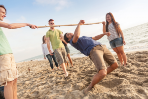 friends playing limbo with a wooden limbo stick on the beach